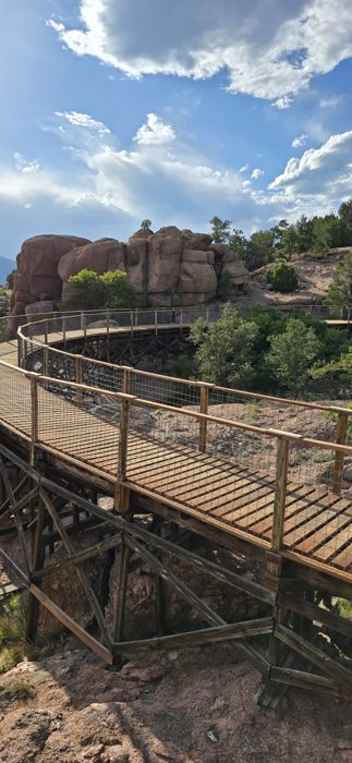 The curving wooden boardwalk winding through red rock formations on the canyon rim.