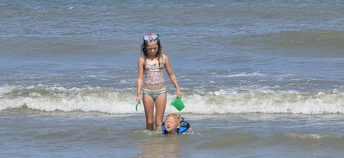 Snorkel mask pushed up on her head, one of the kids picks her way through the breakers while a sibling grins in the surf behind her.
