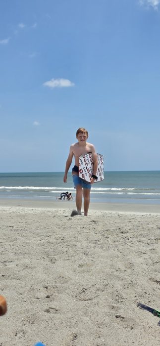Walking up from the surf with the bodyboard tucked under an arm.