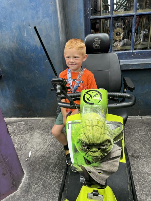 One of the kids grins astride a Yoda-themed mobility scooter outside a shop in the Wizarding World.