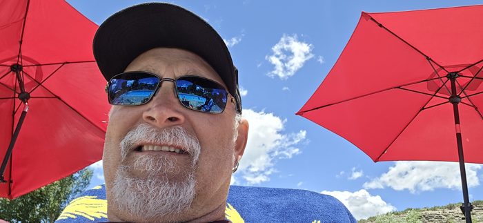 Dad flashes a grin for a solo selfie beneath the red patio umbrella by the pool.