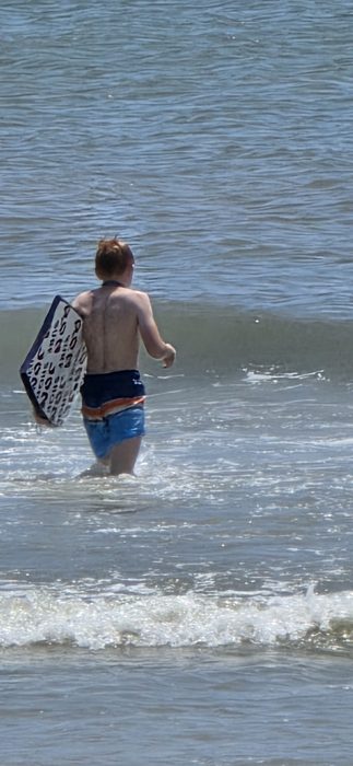 Wading out with the boogie board tucked under an arm, eyeing the next wave.