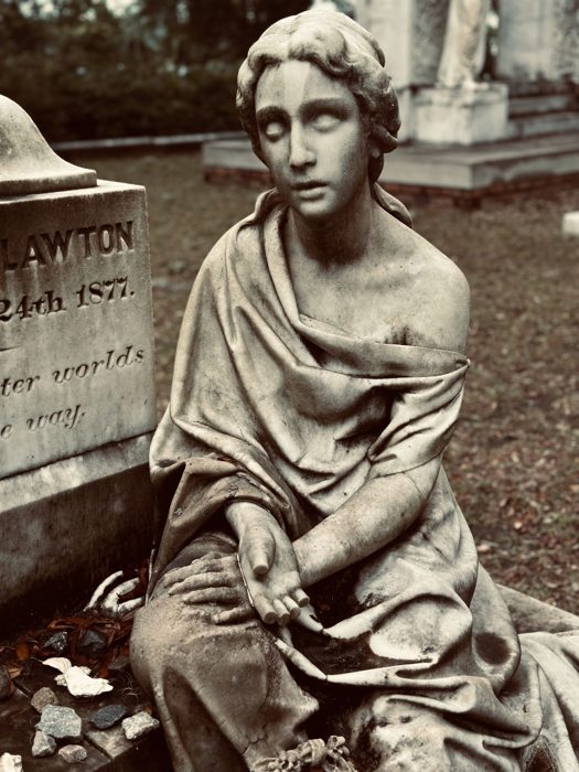 The famous seated maiden statue at Bonaventure Cemetery, framed by old oaks and weathered stone.