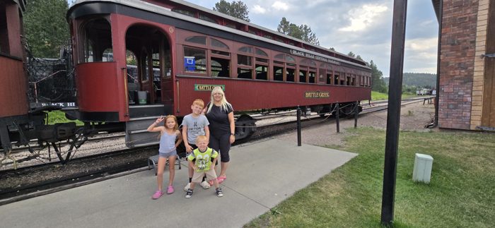 The family poses in front of the vintage maroon passenger cars of the Black Hills steam train.