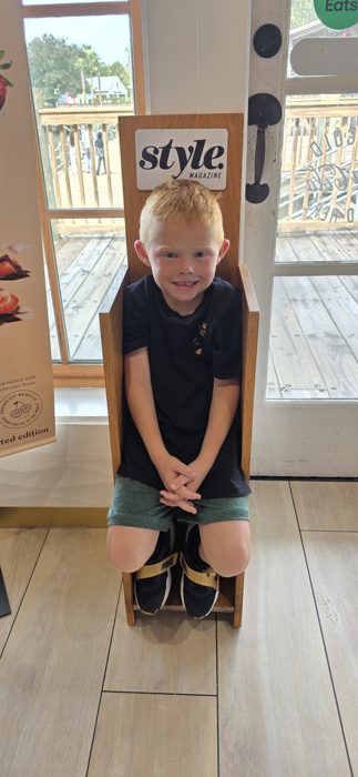 One of the kids poses in a quirky wooden throne chair at a waterfront shop.