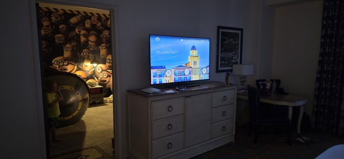 One of the kids peeks into a Minion-themed hideaway room, the TV glowing with a welcome message across the suite.