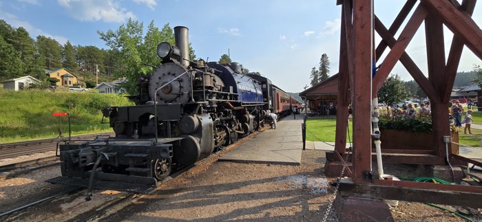 A massive black steam locomotive sitting on the rails beneath the timber trestle at the depot.