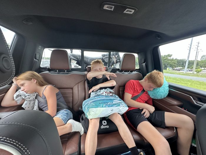 One of the kids strikes a goofy dab in the middle seat while a sibling drifts off against a fuzzy travel pillow.