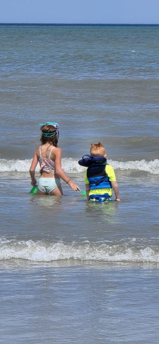 A wide stretch of crowded beach as the kids press on through the waves toward deeper water.