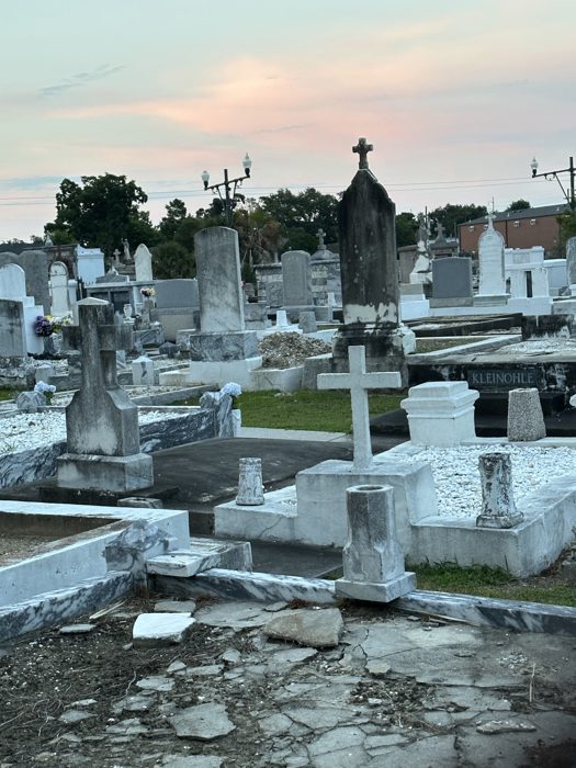 Rows of weathered tombs glow under a soft pastel cemetery sunset.