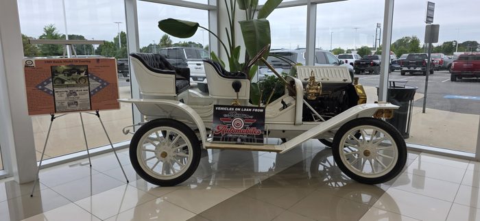 The antique 1909 Buick Model 10 Touring gleams on loan inside the dealership showroom.