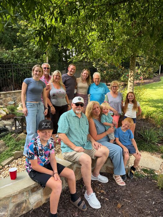 The whole extended family packs onto a garden wall for a group photo under the shade trees.