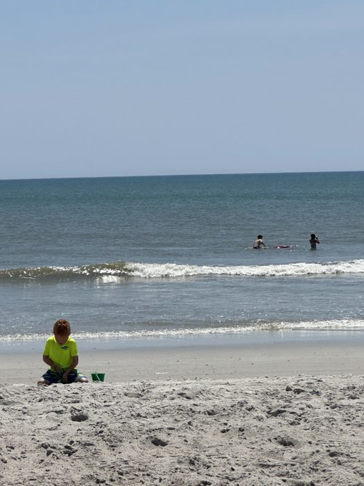 Absorbed in beach digging while two more of the family ride waves out past the break.