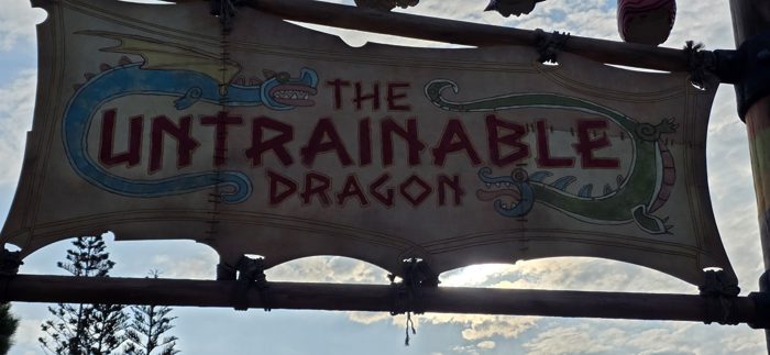 The hand-painted sign for The Untrainable Dragon ride sways overhead against a bright morning sky.