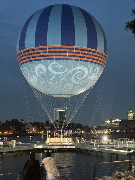 The tethered balloon ride lifts off over the water at Disney Springs as dusk settles in.