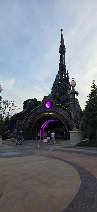 The family strolls through a glowing purple portal beneath a rocky, spired archway as dusk settles over the park.
