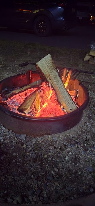 A single log burns bright in the fire ring under a deep dusk sky at the RV site.