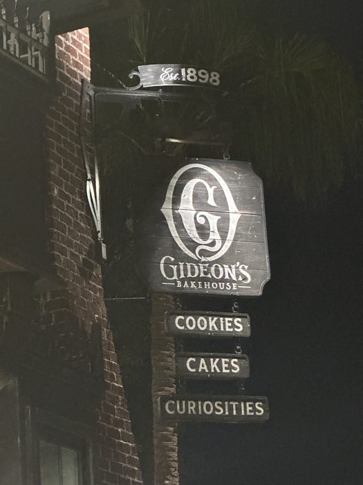 The bakery's vintage hanging sign spells out cookies, cakes, and curiosities against the night sky.