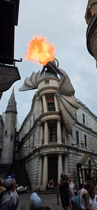 Flames burst from the dragon perched atop Gringotts Bank as the crowd looks up.