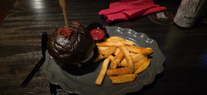A loaded burger with a blackened bun and seasoned fries, plated up for dinner at the park.