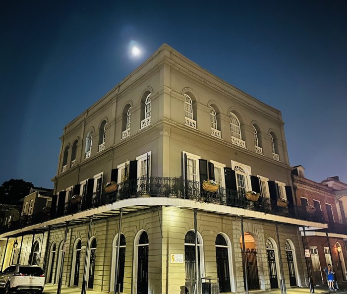 A grand French Quarter corner building glows golden under a full moon.