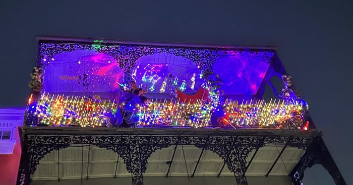A French Quarter balcony strung with vivid Mardi Gras lights and beads.