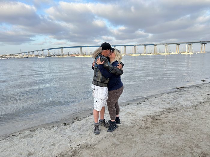 A long, sweet hug on the beach under a wide cloudy sky.