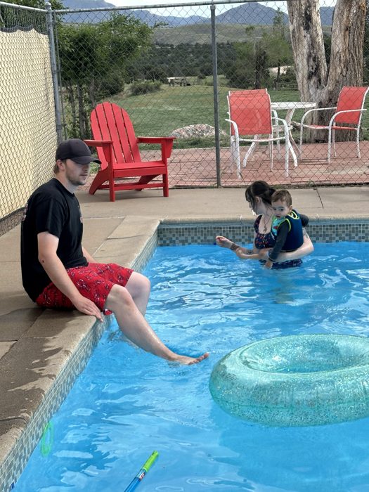 Dad cools his feet in the pool while a little one plays in the inner tube.