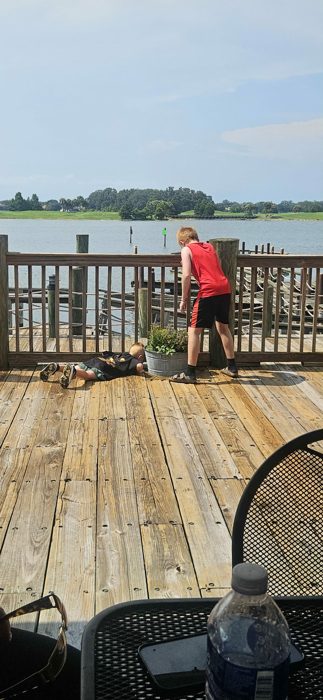 The boys sprawl out on a lakeside dock, one of them flat on his stomach peering over the railing.