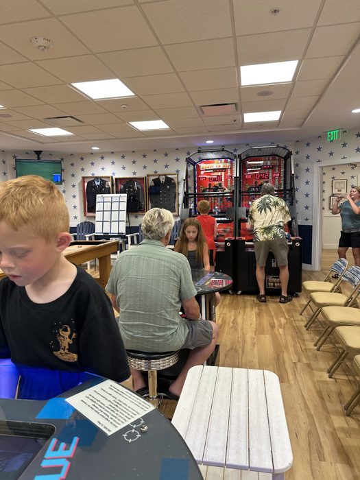 Wide view of the clubhouse game room with the family scattered between arcade machines.