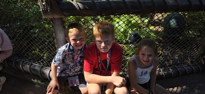 The kids lean in close on the netted queue rail, waiting their turn in the dappled shade.