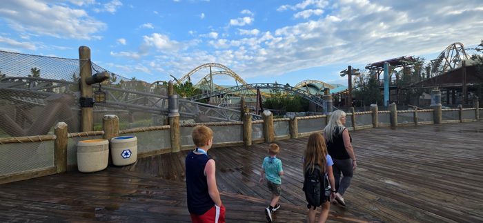 The family strolls the wooden boardwalk with towering coaster tracks looming ahead.