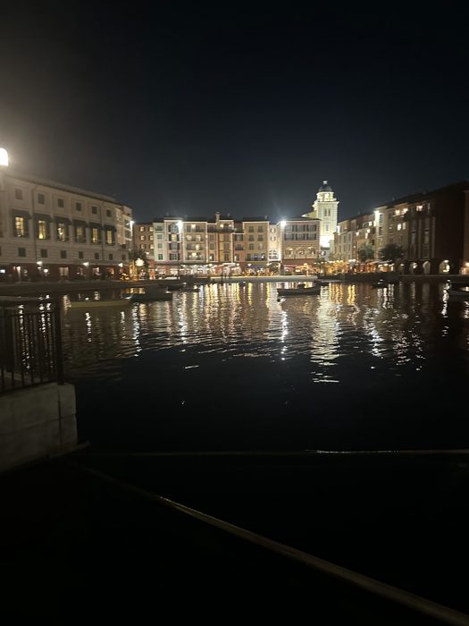The lit-up harborfront glows and reflects across still water on a quiet evening walk.