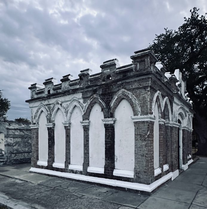 A grand arched mausoleum wall stretches across the cemetery under a moody sky.