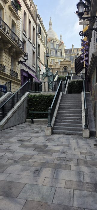 Wand shop signs hang over the quiet Parisian stairway, the distant dome glowing in the morning light.