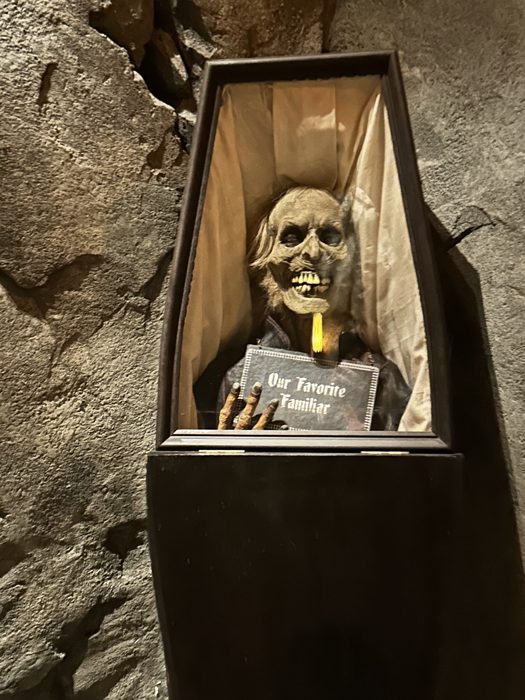 A grinning skeleton in a coffin display labeled Our Favorite Familiar greets guests along the queue.