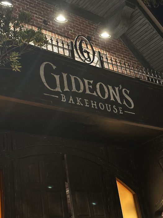 A close-up of the Gideon's Bakehouse sign glowing against the brick under the string lights.