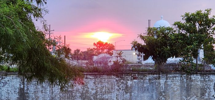 Pink and orange sunset blazing over the old cemetery wall and treeline.
