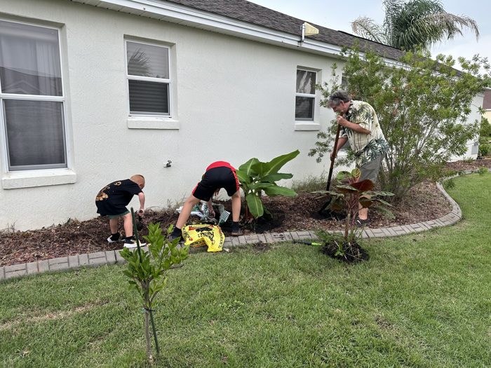 Two of the kids dig in the flower bed while one of the adults breaks ground behind them with a shovel.