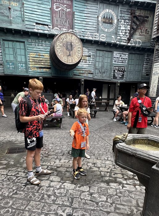 The older two compare notes on their wands outside the Hog's Head Pot in Diagon Alley.