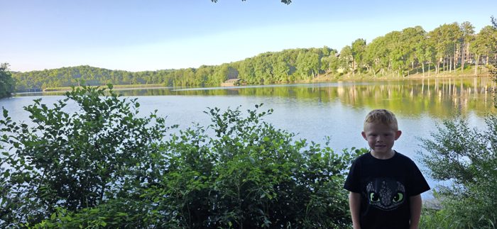 One of the kids pauses lakeside in the early morning quiet, hills glowing on the water behind him.