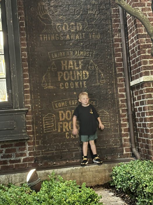 One of the kids poses against Gideon's giant half-pound cookie mural on the brick wall.