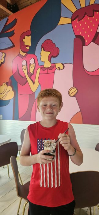 One of the kids grins for a photo with his loaded sundae in front of a colorful ice cream shop mural.