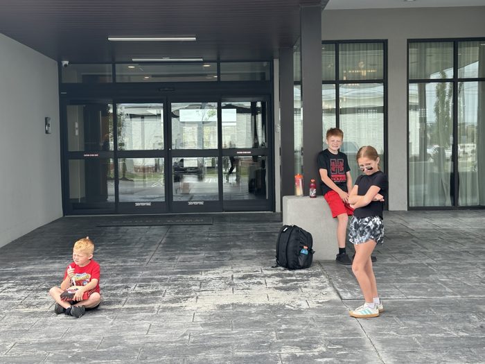 The kids wait out front of the hotel with backpacks and drinks, ready to load up and go.