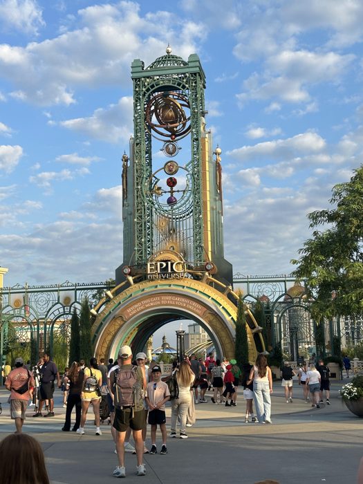 One of the kids poses with a parent in front of the towering Epic Universe clock gate as the morning crowd streams in.