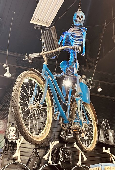 A grinning skeleton pedals a bright blue bicycle in a wonderfully weird French Quarter display.