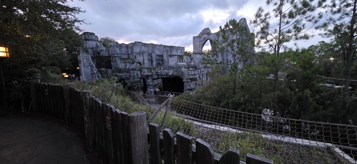 The crumbling ruins above the coaster take on an eerie glow as dusk settles over the park.