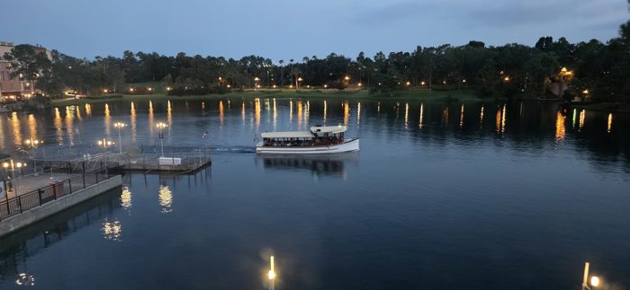 Evening settles over the resort lagoon, the water taxi gliding in as lights begin to glow along the shore.