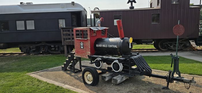 A bright red Black Hills Central display engine parked beside the depot's railcars.