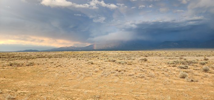 Soft evening light over the sage flats as a distant shower drifts across the mountains beyond camp.